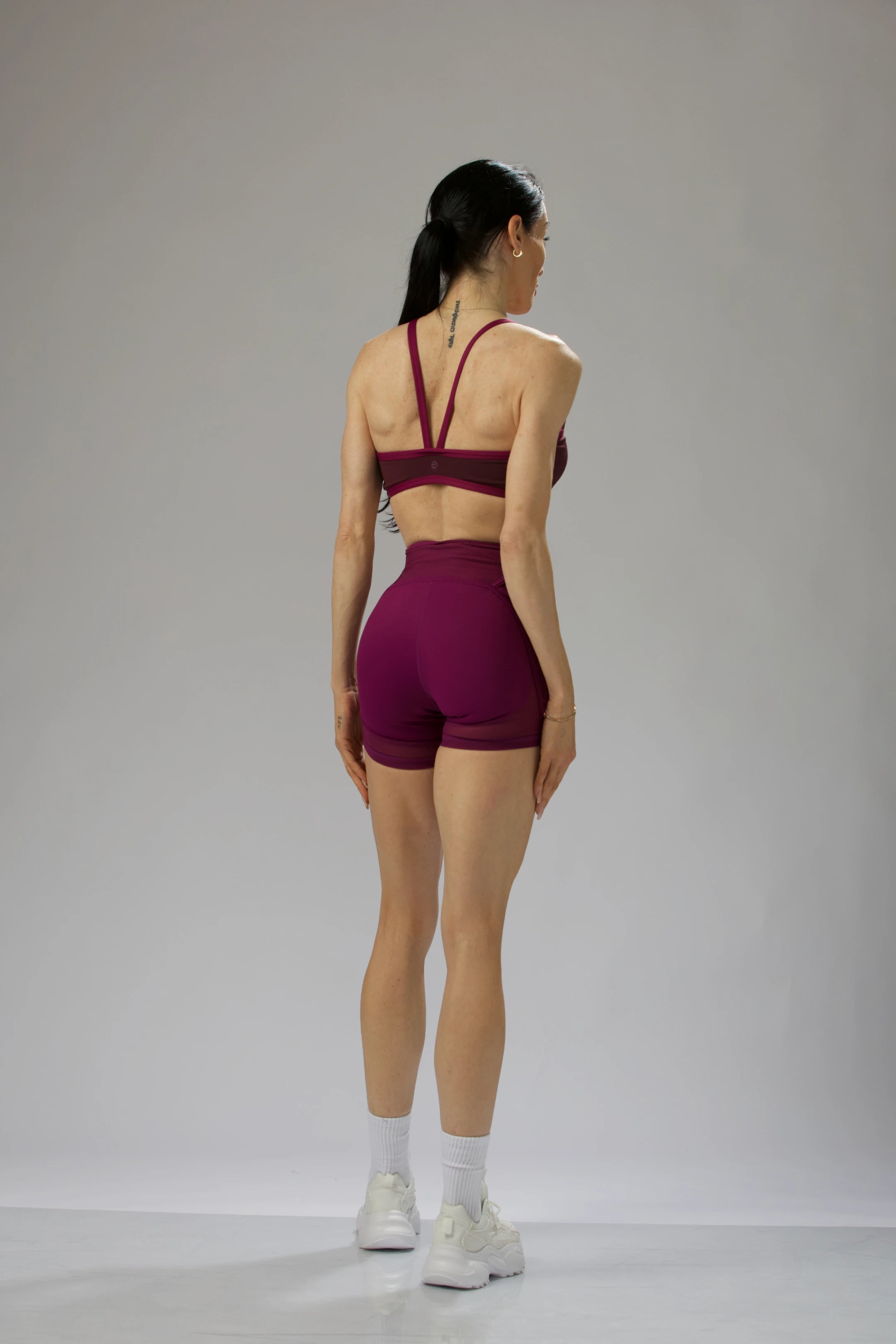 Rear view of a model in a burgundy cutout sports bra and high-waisted shorts, showcasing the cross-back straps.