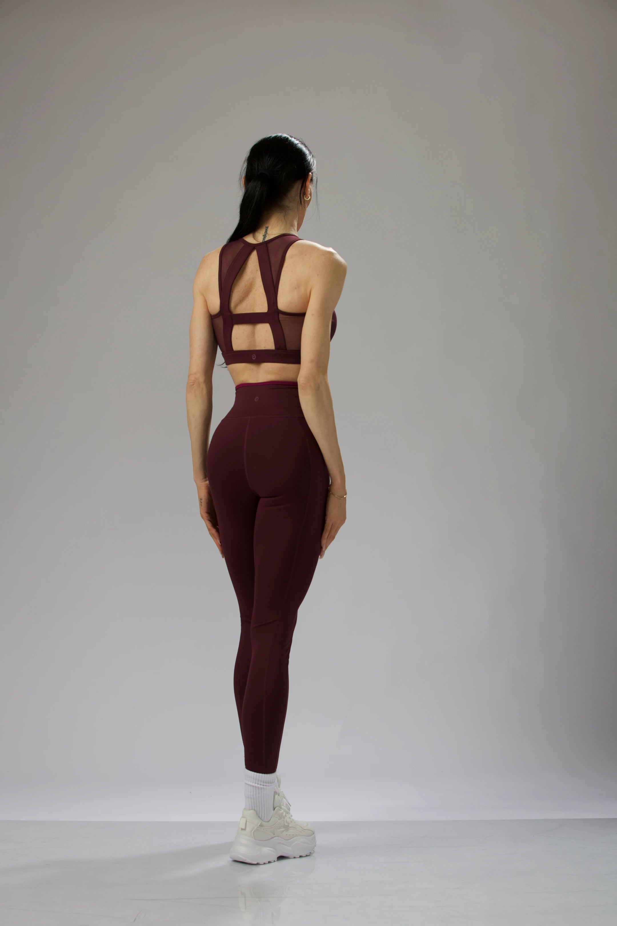Close-up back view of the burgundy sports bra featuring mesh details and a geometric cutout design.