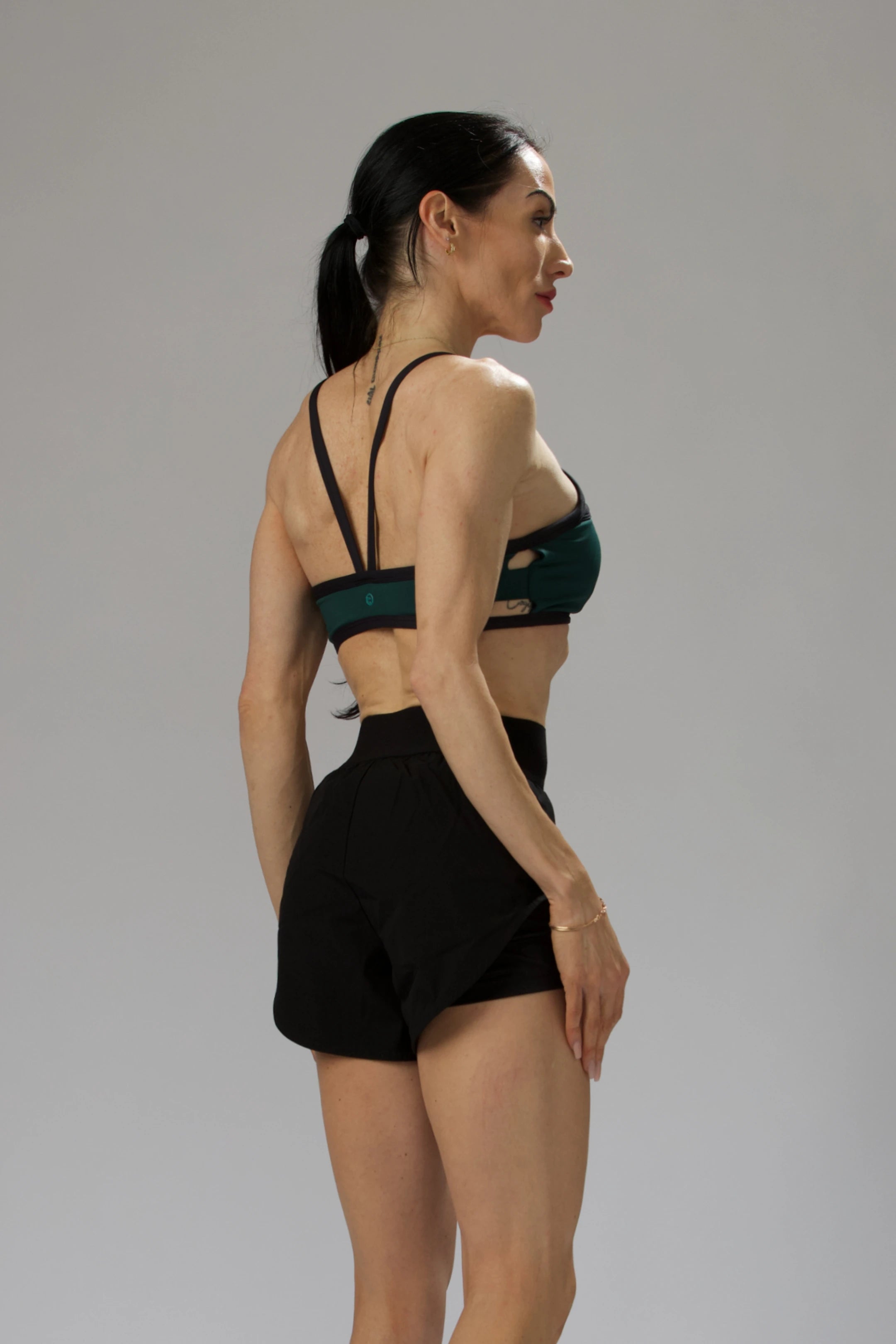 Back view of a model wearing a green and black cutout sports bra and black shorts, showing the strappy back design.