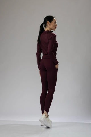 Front view of a woman wearing a dark purple fitted long sleeve top and matching leggings, styled for activewear.
