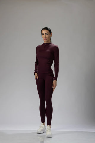 Front view of a woman wearing a dark purple merlot fitted long sleeve top and matching leggings, styled for activewear.
