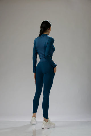 Front view of a woman wearing a dark teal fitted long sleeve top and matching leggings, styled for activewear.
